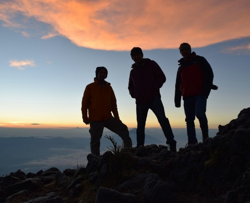 silhouette of 2 men standing on rocky shore during sunset